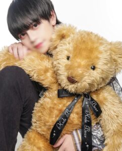 Young person cuddling a large golden teddy bear with a black ribbon reading 'Kids Bear'.