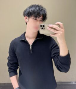 Person takes a mirror selfie with a gold iPhone, wearing a dark navy half-zip sweater and white AirPods; face blurred for privacy.