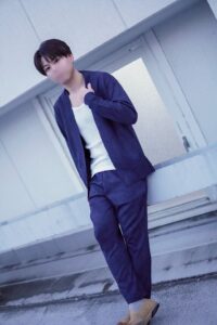 Young man in a navy suit with a white shirt stands on concrete stairs, adjusting his jacket.