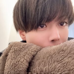 Close-up of a person with dark hair, eyes peeking over a plush beige blanket.