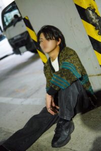 Person sits on a concrete floor in a dim parking garage, leaning against a yellow-and-black striped pillar near a vehicle behind them.