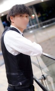 Young man in a white dress shirt and black waistcoat leaning on a glass railing indoors.