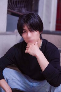 Young man sits on stairs with his hand resting on his chin, wearing a black long-sleeve shirt and light jeans (casual portrait).