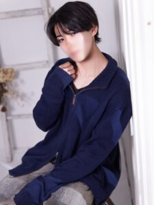 Young person with blurred face wearing a navy zip sweater, sitting by a white doorframe in a casual pose.